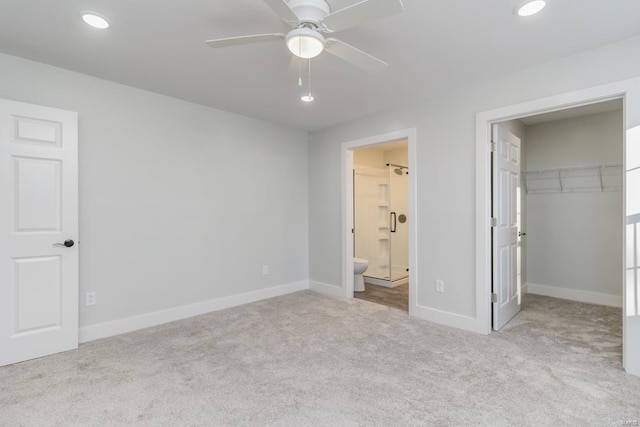 unfurnished bedroom featuring light carpet, ceiling fan, ensuite bath, a walk in closet, and a closet