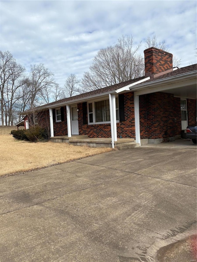 ranch-style house with covered porch, brick siding, concrete driveway, a carport, and a chimney