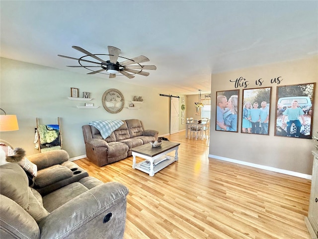 living room with light wood-type flooring, ceiling fan, and a barn door