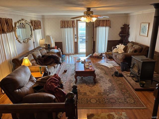 living room with wood-type flooring, ceiling fan, a wood stove, and crown molding