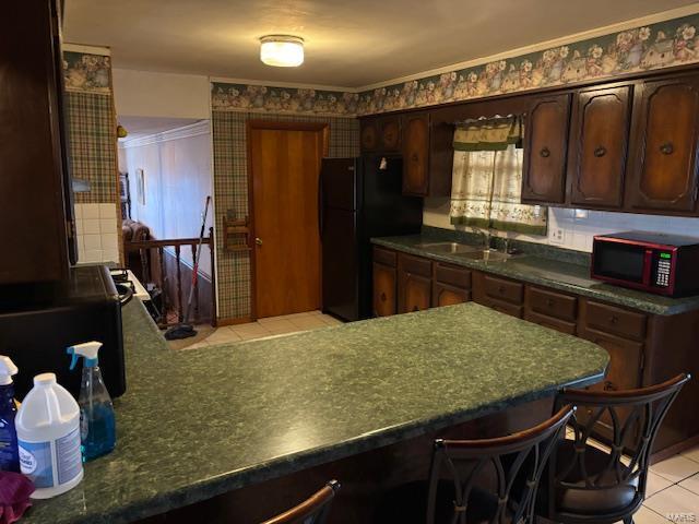 kitchen featuring sink, dark brown cabinetry, light tile patterned floors, and black fridge