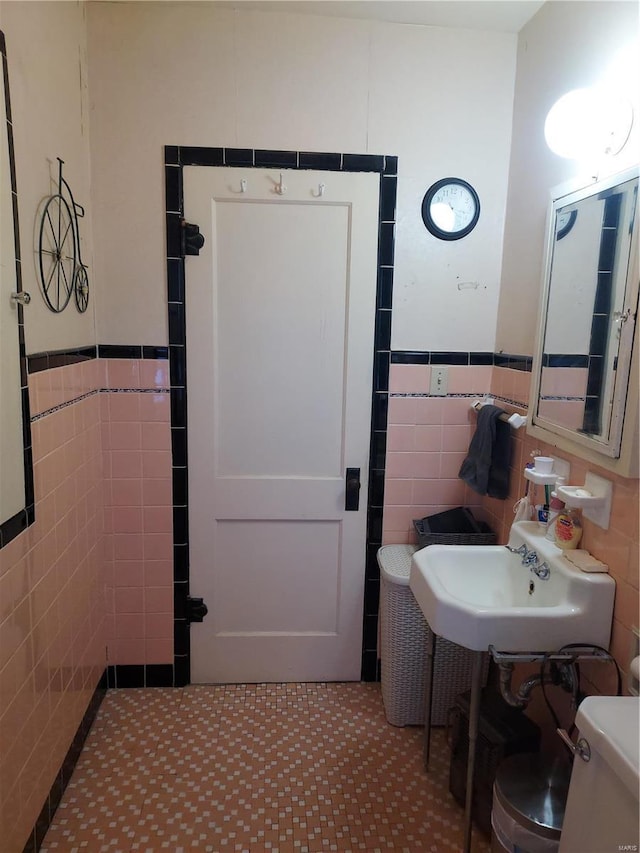 bathroom with toilet, tile patterned flooring, sink, and tile walls