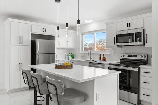 kitchen with appliances with stainless steel finishes, a kitchen island, decorative light fixtures, white cabinetry, and tasteful backsplash