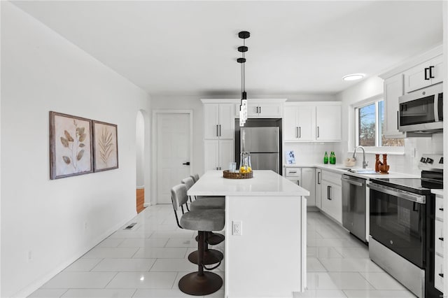 kitchen with white cabinets, a kitchen island, decorative light fixtures, backsplash, and stainless steel appliances