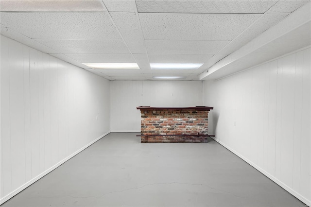 basement with wood walls, bar area, and a drop ceiling