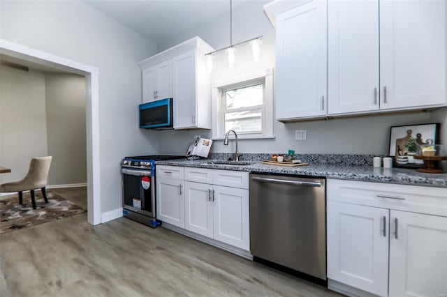 kitchen with light hardwood / wood-style floors, appliances with stainless steel finishes, sink, white cabinets, and pendant lighting