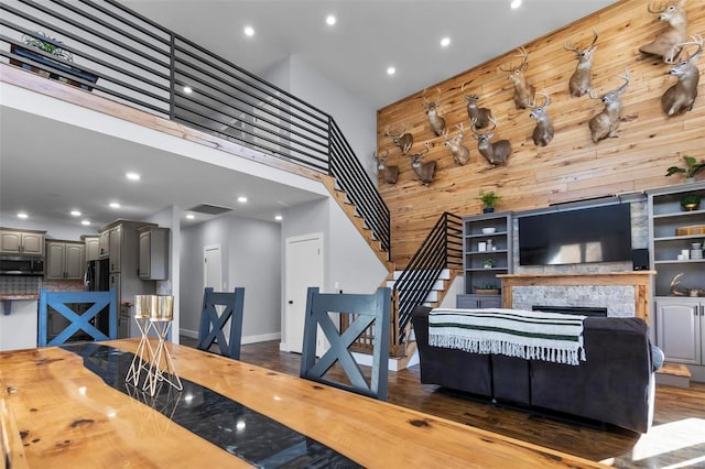 dining room with a high ceiling, dark hardwood / wood-style floors, a fireplace, and wooden walls