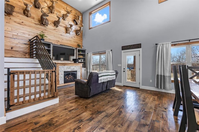 unfurnished living room featuring dark wood-type flooring, wooden walls, a fireplace, and a high ceiling