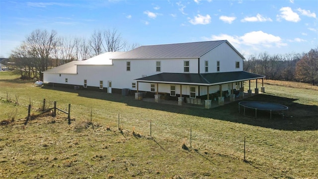 rear view of property with a trampoline and a lawn