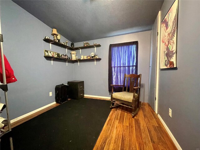 living area featuring a textured ceiling, baseboards, and wood finished floors