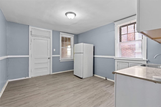 kitchen featuring white cabinetry, sink, white fridge, and light wood-type flooring