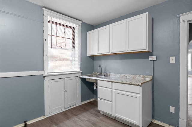 kitchen with white cabinetry, sink, light wood-type flooring, and a wealth of natural light