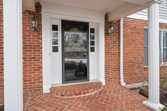 view of exterior entry with brick siding and a porch