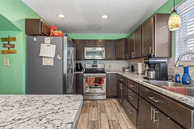 kitchen with sink, decorative light fixtures, dark brown cabinets, stainless steel appliances, and light hardwood / wood-style floors