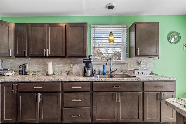 kitchen with decorative light fixtures, light stone countertops, sink, and dark brown cabinets