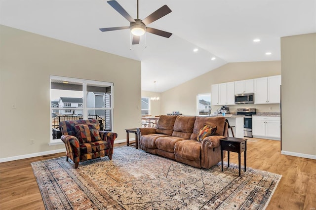 living room with ceiling fan with notable chandelier, vaulted ceiling, and light hardwood / wood-style floors