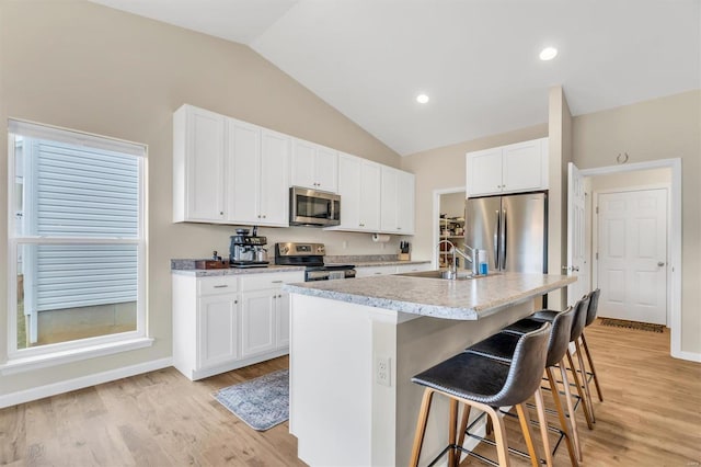 kitchen with sink, a breakfast bar, a kitchen island with sink, white cabinetry, and stainless steel appliances