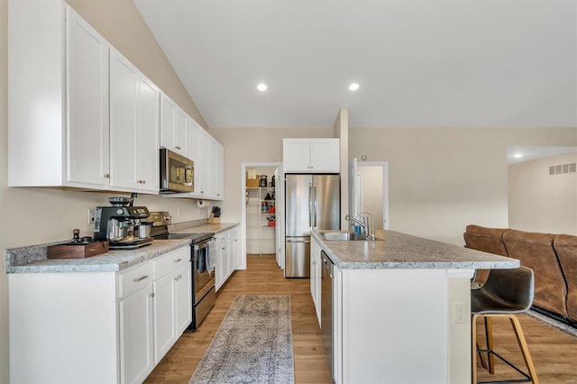 kitchen with appliances with stainless steel finishes, sink, white cabinets, a kitchen bar, and a kitchen island with sink