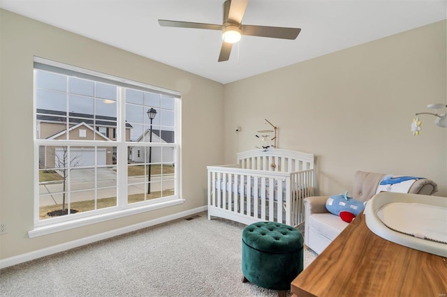 carpeted bedroom featuring a nursery area and ceiling fan