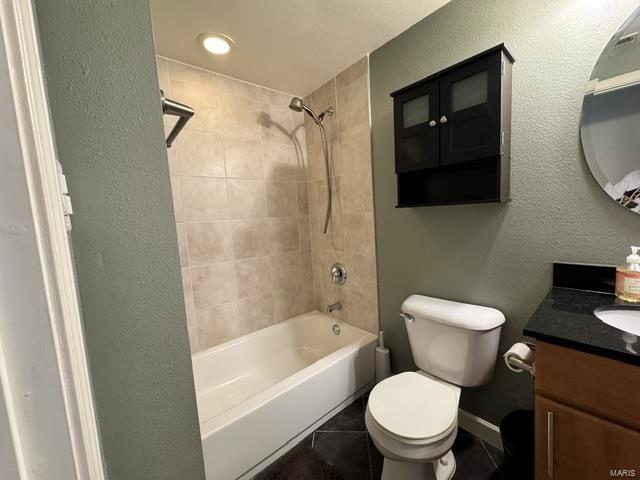 full bathroom featuring vanity, tiled shower / bath, tile patterned floors, and toilet