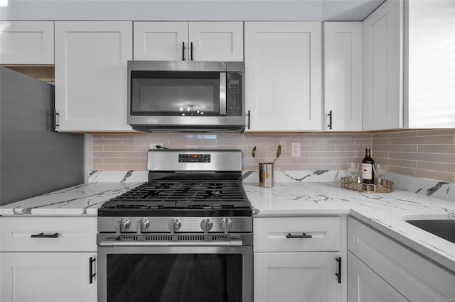 kitchen with sink, white cabinetry, backsplash, stainless steel appliances, and light stone counters