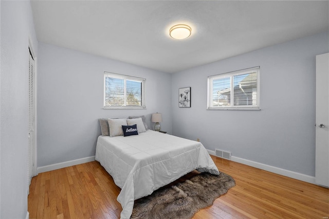 bedroom with multiple windows, light wood-type flooring, and a closet