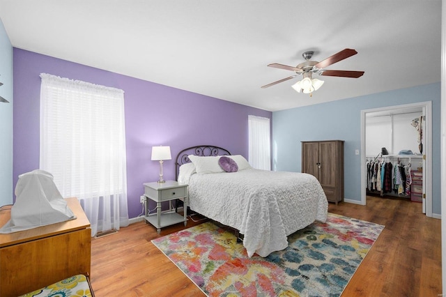 bedroom with a walk in closet, wood-type flooring, a closet, and ceiling fan