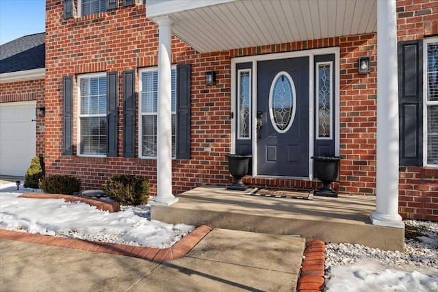 snow covered property entrance featuring a porch and a garage