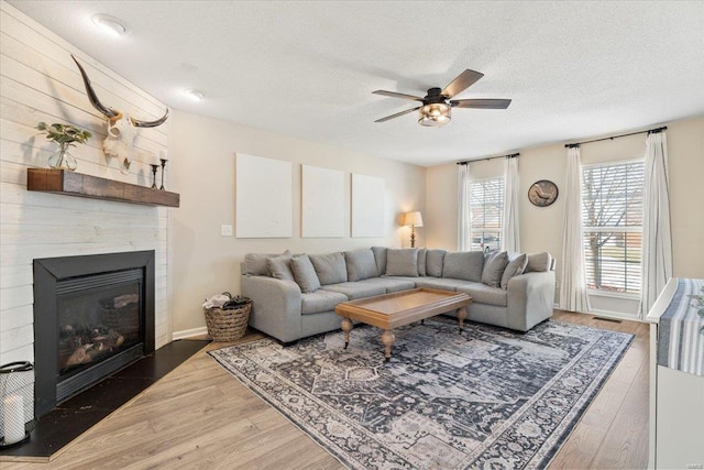 living room featuring ceiling fan, a fireplace, dark hardwood / wood-style flooring, and a textured ceiling