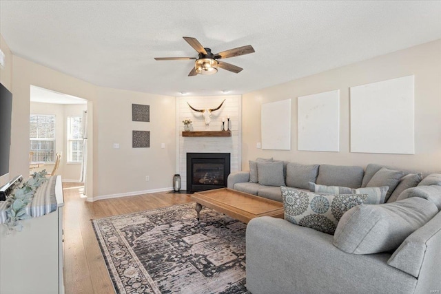 living room with ceiling fan, a textured ceiling, a brick fireplace, and light wood-type flooring