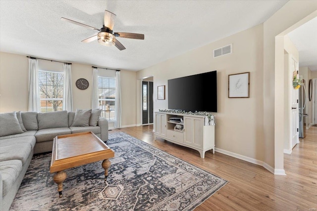 living room with ceiling fan, a textured ceiling, and light wood-type flooring