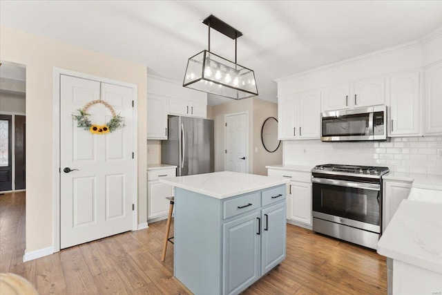 kitchen featuring appliances with stainless steel finishes, backsplash, a center island, white cabinets, and decorative light fixtures