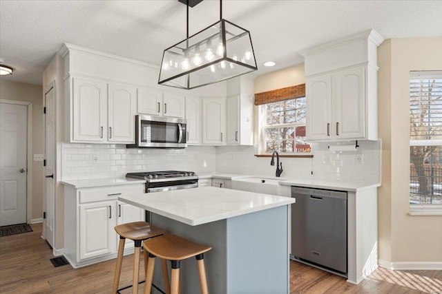 kitchen featuring a kitchen island, appliances with stainless steel finishes, decorative light fixtures, white cabinetry, and light hardwood / wood-style floors