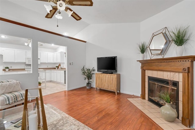 living room with light wood-type flooring, ceiling fan, vaulted ceiling, and a fireplace