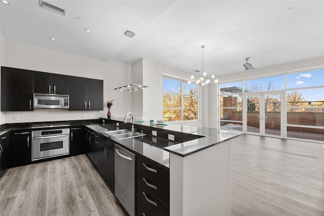 kitchen featuring appliances with stainless steel finishes, decorative light fixtures, sink, light wood-type flooring, and an inviting chandelier