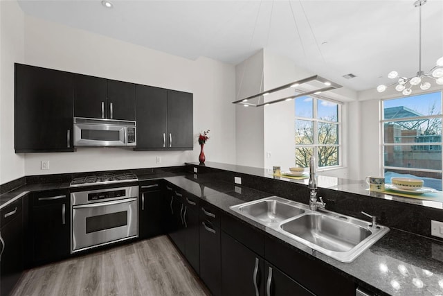 kitchen with sink, dark stone countertops, hanging light fixtures, light hardwood / wood-style floors, and stainless steel appliances