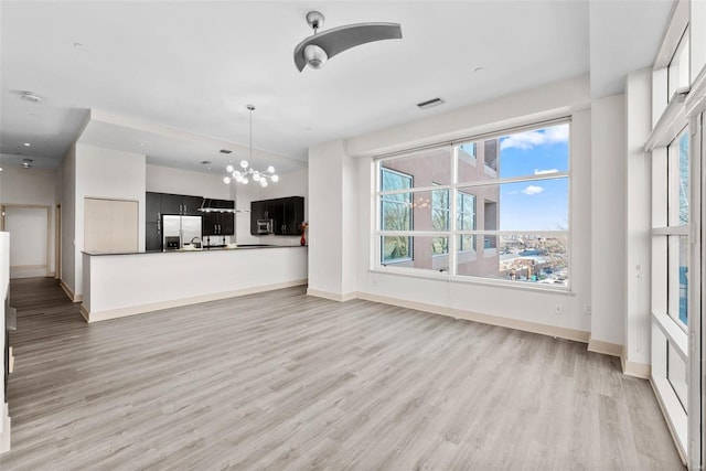 unfurnished living room with an inviting chandelier, sink, and light wood-type flooring