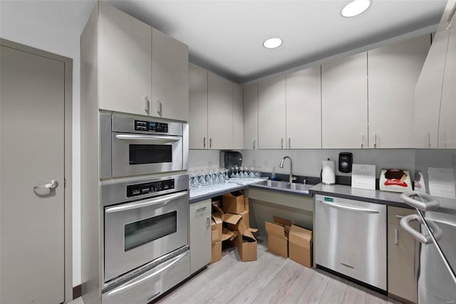 kitchen with appliances with stainless steel finishes, sink, gray cabinetry, and light wood-type flooring