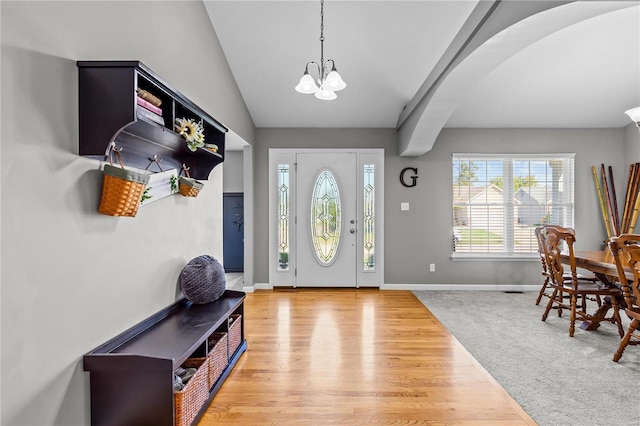 entrance foyer featuring baseboards, arched walkways, lofted ceiling, wood finished floors, and an inviting chandelier