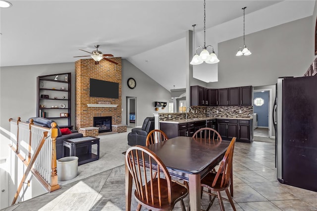 dining area with ceiling fan, high vaulted ceiling, light tile patterned floors, and a brick fireplace