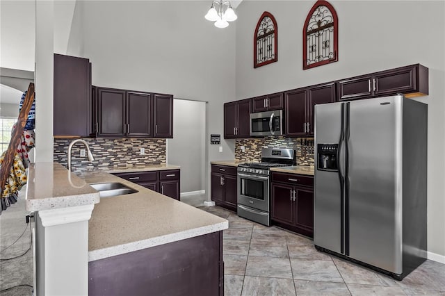 kitchen with a peninsula, a high ceiling, a sink, appliances with stainless steel finishes, and light stone countertops