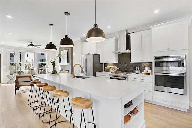 kitchen with pendant lighting, white cabinetry, a kitchen island with sink, stainless steel appliances, and wall chimney range hood