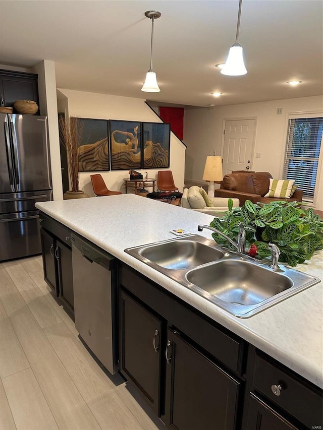 kitchen with stainless steel appliances, decorative light fixtures, sink, and light wood-type flooring