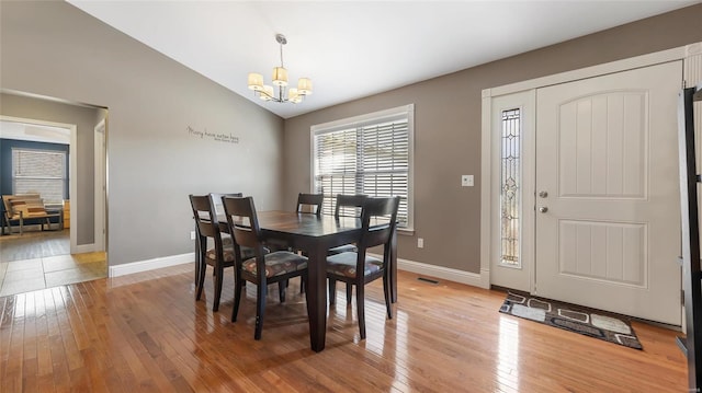 dining area with an inviting chandelier, wood-type flooring, and vaulted ceiling