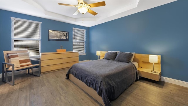 bedroom featuring hardwood / wood-style floors, a raised ceiling, and ceiling fan