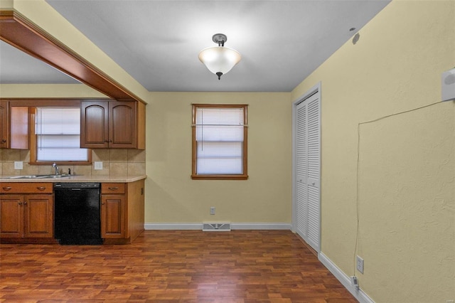 kitchen featuring black dishwasher, sink, dark hardwood / wood-style flooring, backsplash, and plenty of natural light