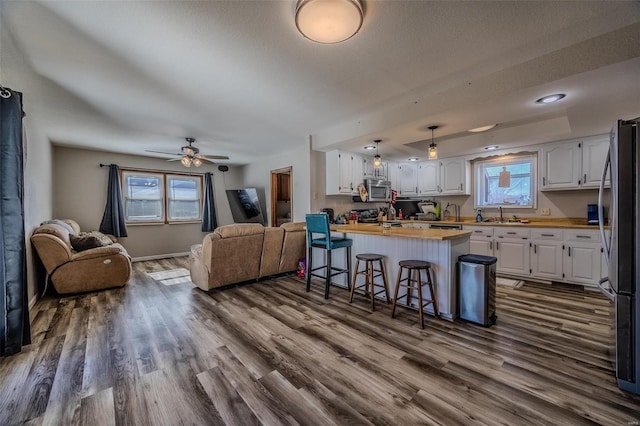 kitchen with appliances with stainless steel finishes, hardwood / wood-style floors, butcher block counters, white cabinets, and a kitchen bar