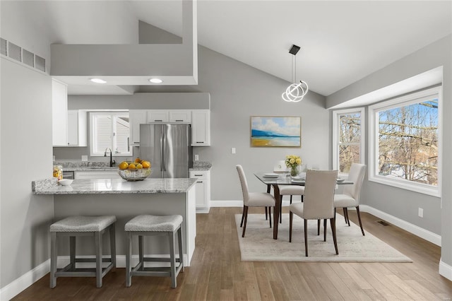 kitchen with high vaulted ceiling, decorative light fixtures, white cabinetry, stainless steel fridge, and light stone counters