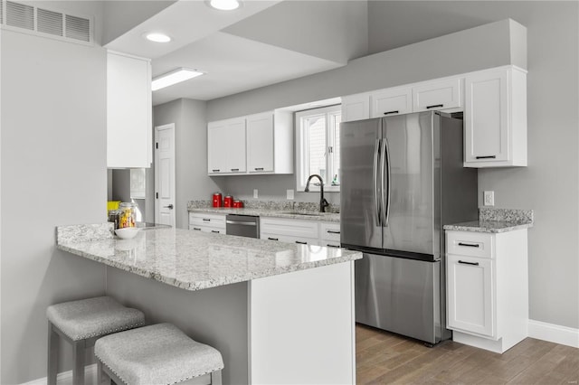 kitchen with white cabinetry, light stone counters, appliances with stainless steel finishes, a kitchen breakfast bar, and kitchen peninsula