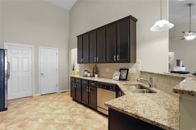 kitchen with appliances with stainless steel finishes, sink, decorative light fixtures, a towering ceiling, and light stone countertops